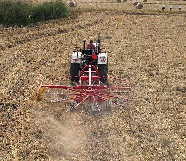 Tractor pulling a Kisani baler through a harvested field with hay bales